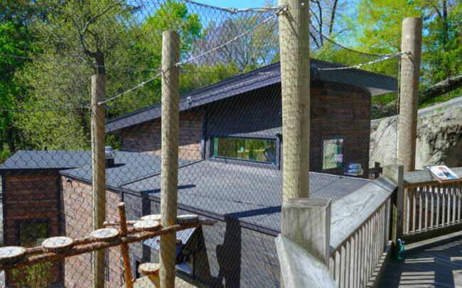 A wooden cabin-like structure with a slanted roof and a deck. The structure is surrounded by a wire fence and wooden posts, creating an enclosed, protected area.