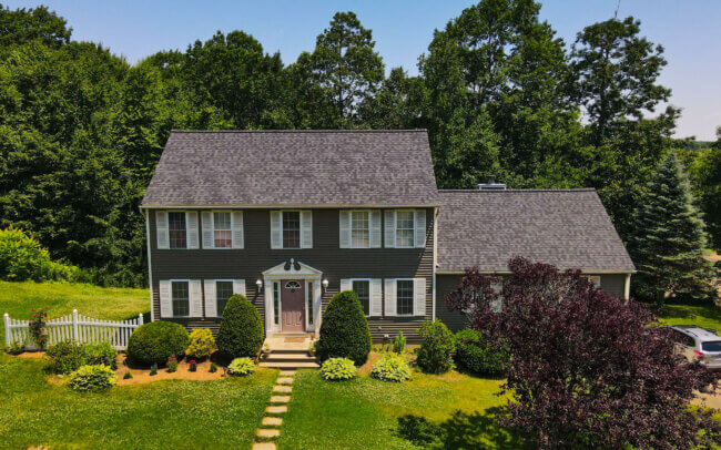 Aerial view of a large two-story house with a dark gray roof, surrounded by a well-manicured yard and trees.