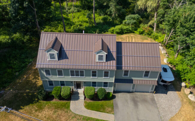 An aerial view of a large, two-story house with a red tile roof, surrounded by trees and a grassy yard.